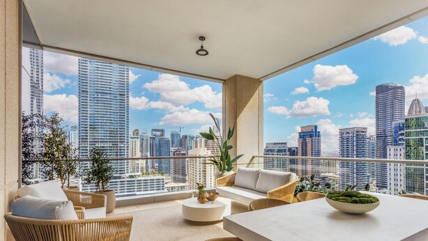 A balcony with a city view, wicker furniture, a round table, and potted plants. - LUX  The Aurora Marina View Suite (Dubai)