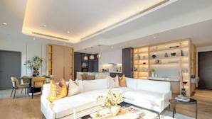 A modern living room with a white sofa, dining area, kitchen, and a well-lit shelving unit. - LUX  The Aurora Marina View Suite (Dubai)