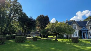 A well-maintained lawn, a large tree, and a stone building with a blue door.