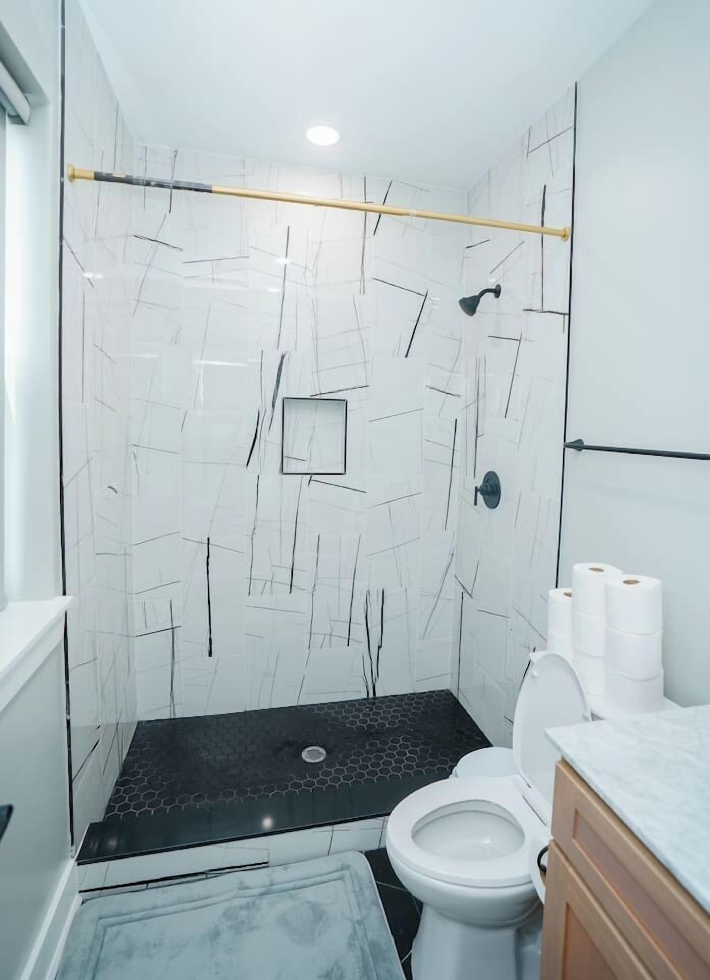 Et badeværelse med en hvid flisevæg, mørkt gulv, et hvidt toilet og en trækommode.
