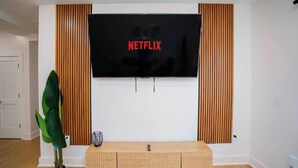 Ein modernes Wohnzimmer mit einem an der Wand befestigten Flachbildfernseher, einem Holzkonsolentisch und einem Topfpflanzen.