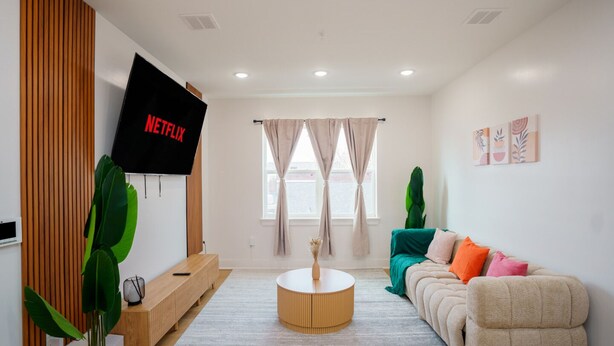 Ein modernes Wohnzimmer mit Flachbildfernseher, einer Couch, einem Couchtisch und einer großen Pflanze.