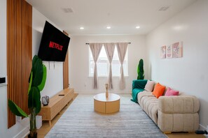 A modern living room with a flat-screen TV, a sofa, a coffee table, and a large plant. - Modern Home | Arcade + Rooftoop | 30m to NYC (Jersey City)