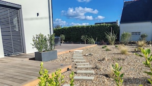 A modern outdoor area with a wooden deck, a stone pathway, and various plants. - Architect-designed villa near the beach Trévignon -South Brittany -France (Trégunc)