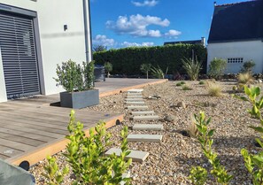 Ein moderner Außenbereich mit Holzterrasse, Kiesweg und verschiedenen Pflanzen.