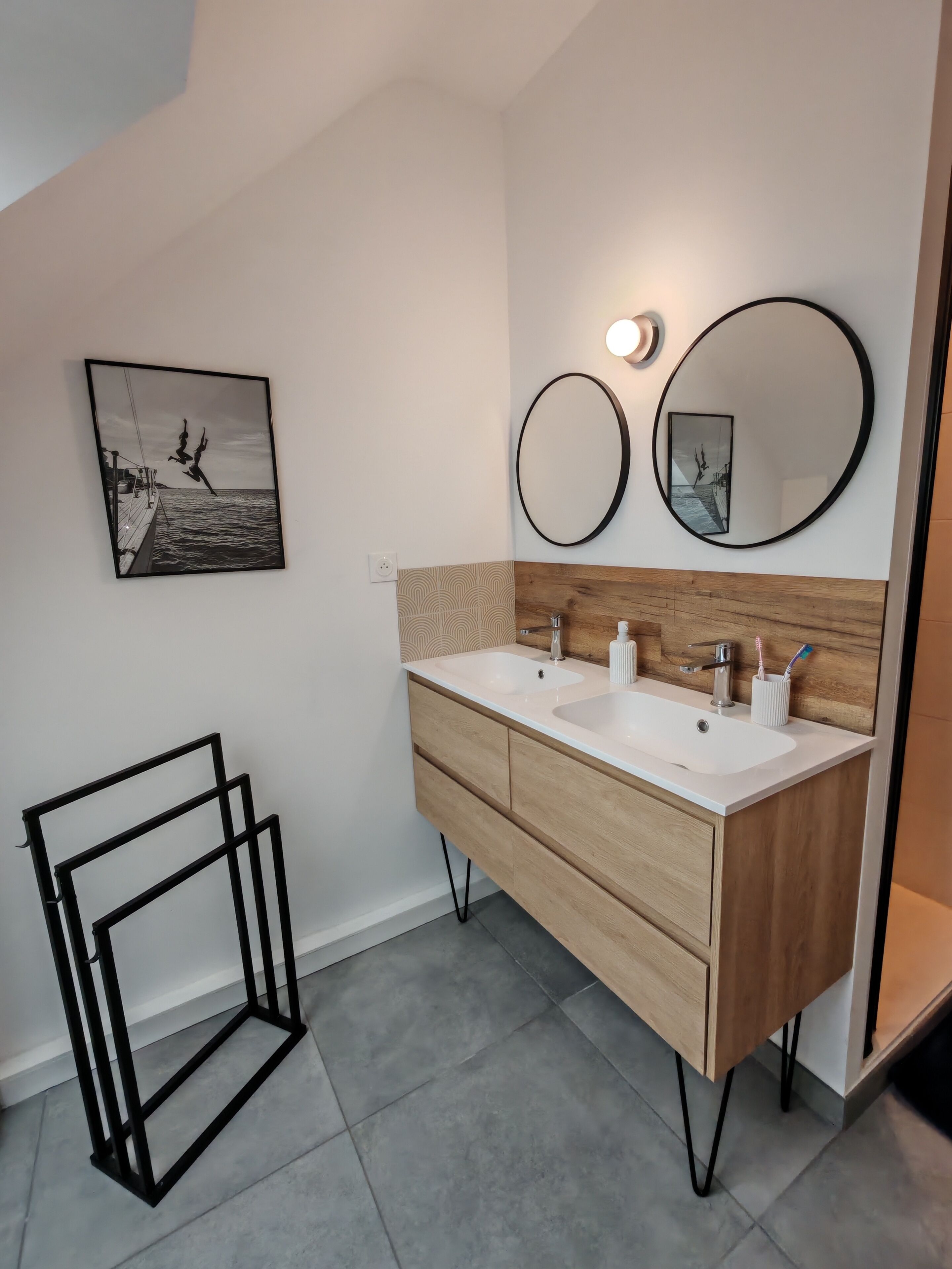 A modern bathroom with two sinks, a wooden vanity, a large mirror, and a framed picture on the wall.