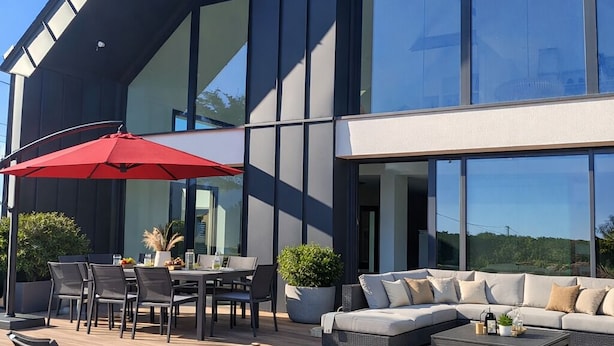 A modern outdoor seating area with a dining table, chairs, and a red umbrella. - Architect-designed villa near the beach Trévignon -South Brittany -France (Trégunc)