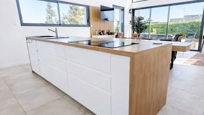 A modern kitchen with a large island, white cabinetry, and a view of the outdoors. - Architect-designed villa near the beach Trévignon -South Brittany -France (Trégunc)