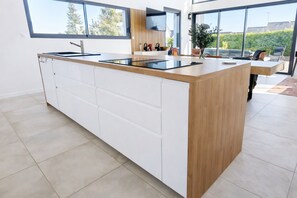 Eine moderne Küche mit einer großen Kochinsel, weißen Schränken und Blick ins Freie.
