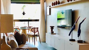 Uma sala de estar moderna com um sofá, uma mesa de jantar e uma TV fixada na parede.