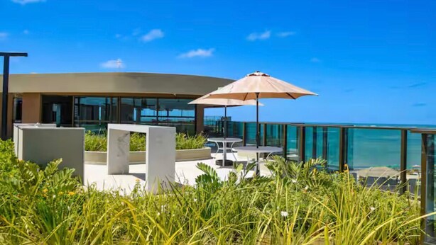 Uma área moderna de estar ao ar livre com guarda-corpo de vidro e vista para o mar.