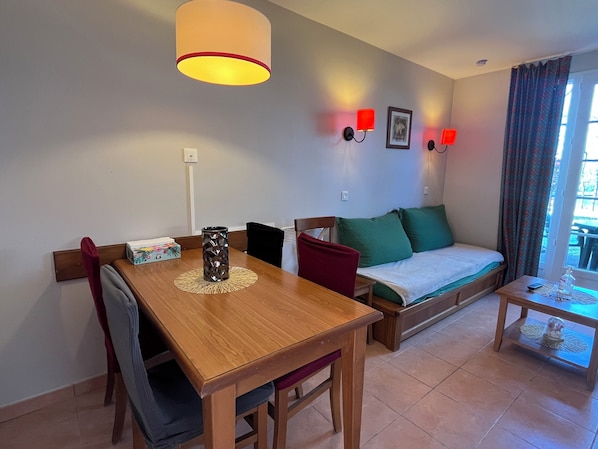 Une pièce comprenant une table à manger en bois, un canapé avec des coussins verts, une petite table d’appoint et une lampe.