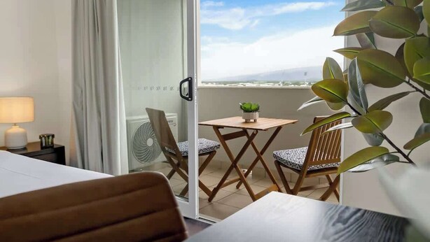 Ein Balkon mit Blick, einem Tisch mit Stühlen, einem Blumentopf und einem Ventilator.