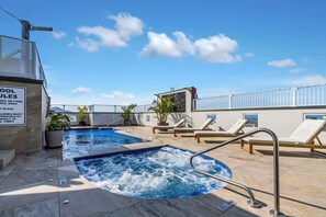 Una piscina en la azotea con sillas de descanso, un jacuzzi y un cartel con las normas de la piscina.
