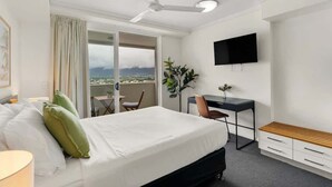 A hotel room with a bed, a desk, a chair, a TV, and a balcony with a view. - Explore Cairns Esplanade from your Private Studio (Cairns)