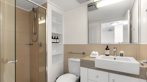 A modern bathroom with a glass-enclosed shower, a toilet, a sink with toiletries, and a mirror. - Explore Cairns Esplanade from your Private Studio (Cairns)