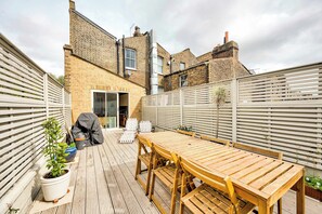 A wooden deck with a table and chairs, a potted plant, and a barbecue grill. - The Sun Deck Townhouse (Greater London)