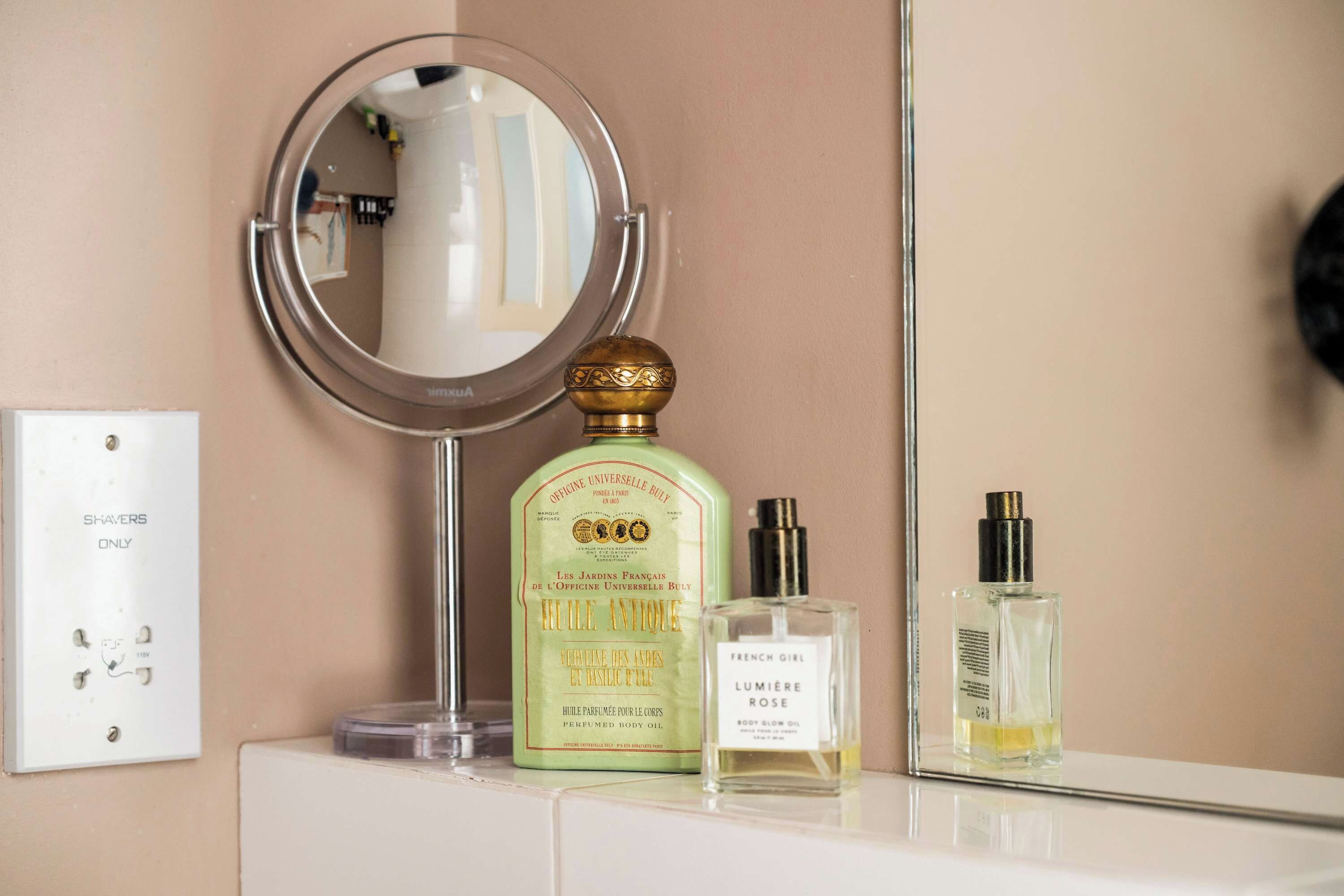 A bathroom vanity with a round mirror, a bottle of perfume, and a bottle of body oil.