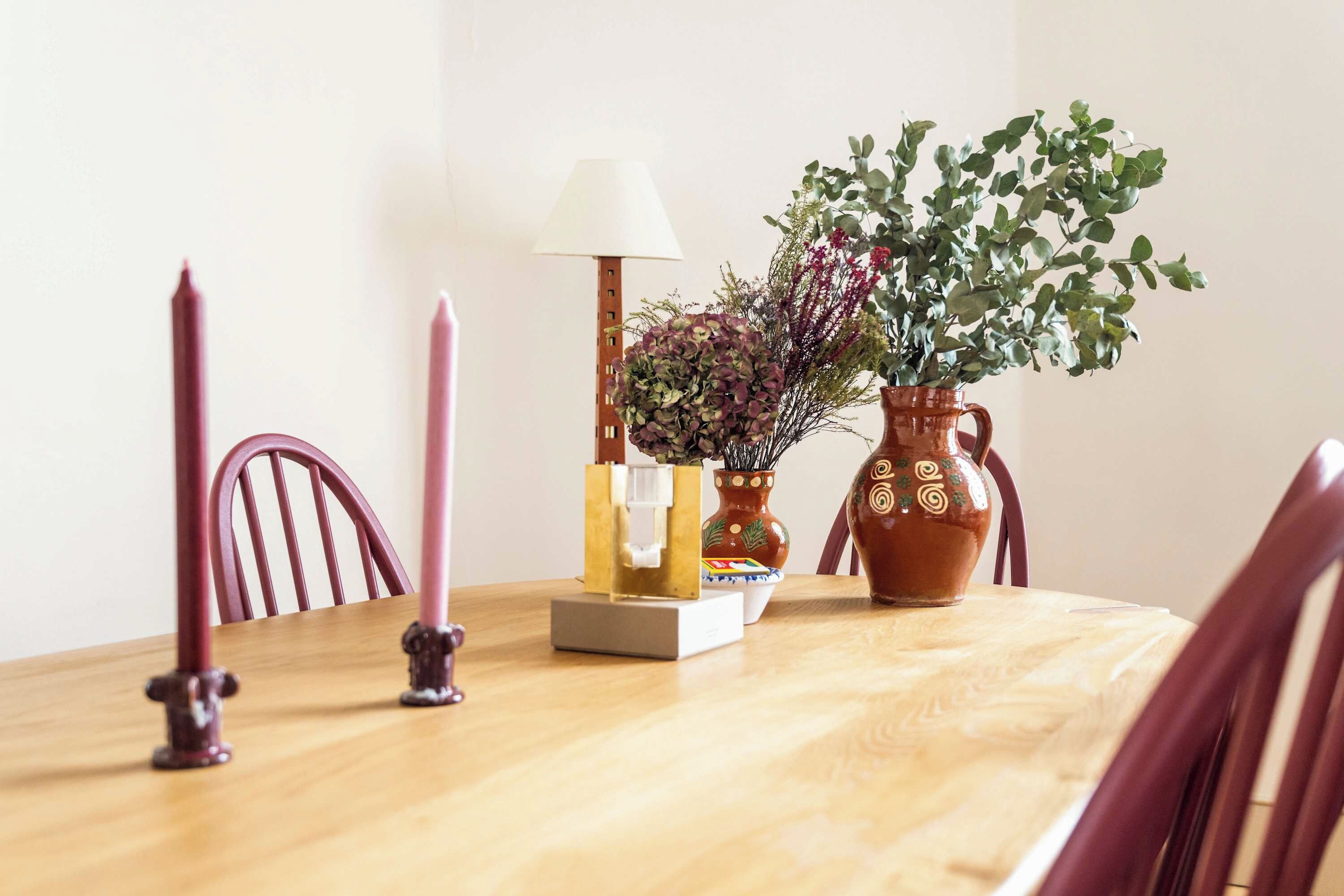 Een houten eettafel met een lamp, kaarsen, een vaas met planten en een decoratieve doos.
