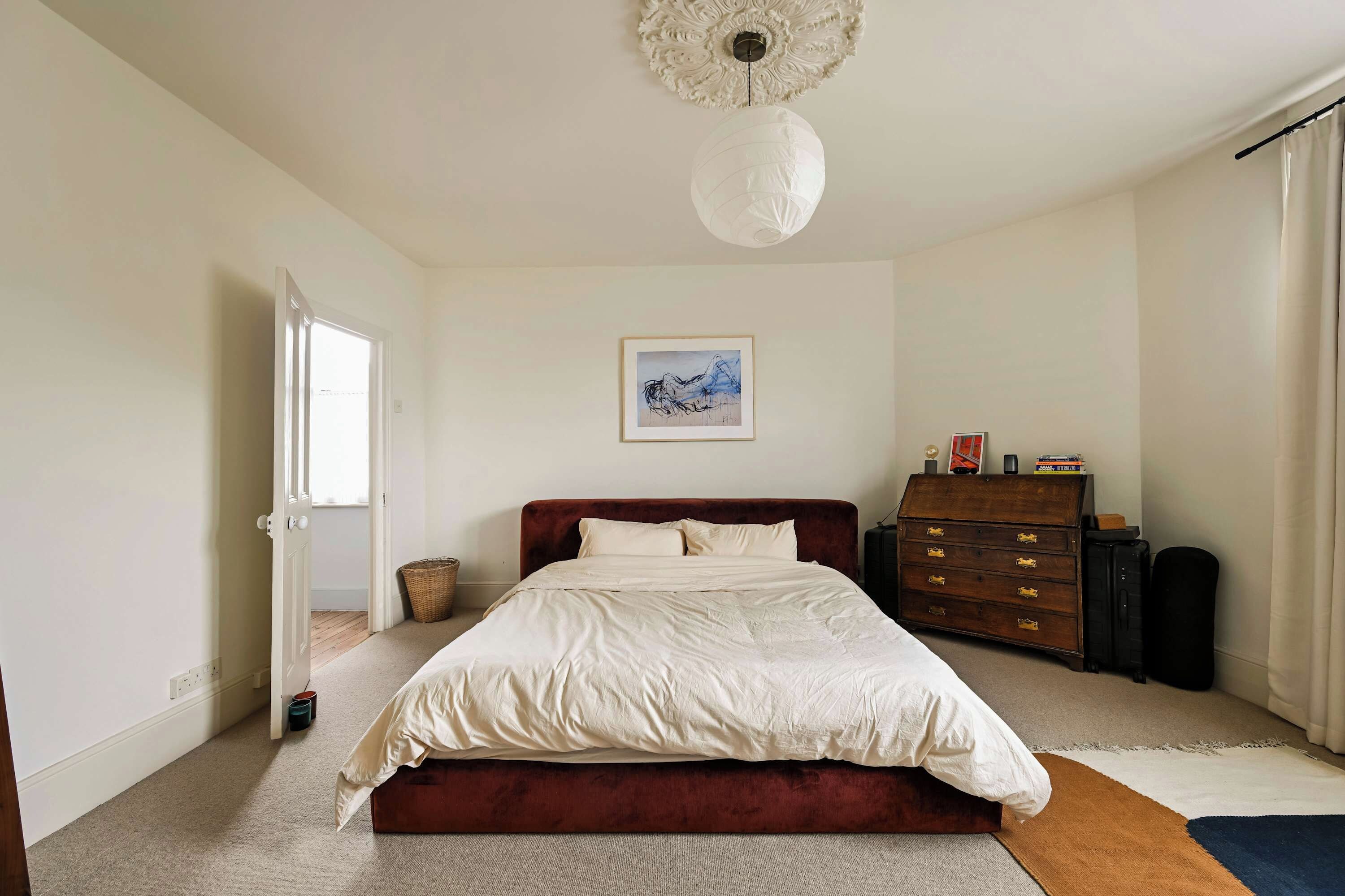 A bedroom with a bed, a dresser, a lamp, and a painting on the wall.