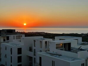 A modern building complex with multiple white structures, some with balconies, and a sunset over the sea in the background. - Vista Bonita | Ocean Views | 2 King Suites (Cabo San Lucas)