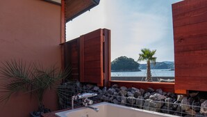 A bathroom with a bathtub, a potted plant, and a view of a body of water and palm tree.