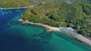 An aerial view of a coastal area with a boat dock, clear turquoise waters, and dense greenery.