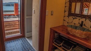 A bathroom with a stone wall, wooden vanity, and a view of a beach through an open door.