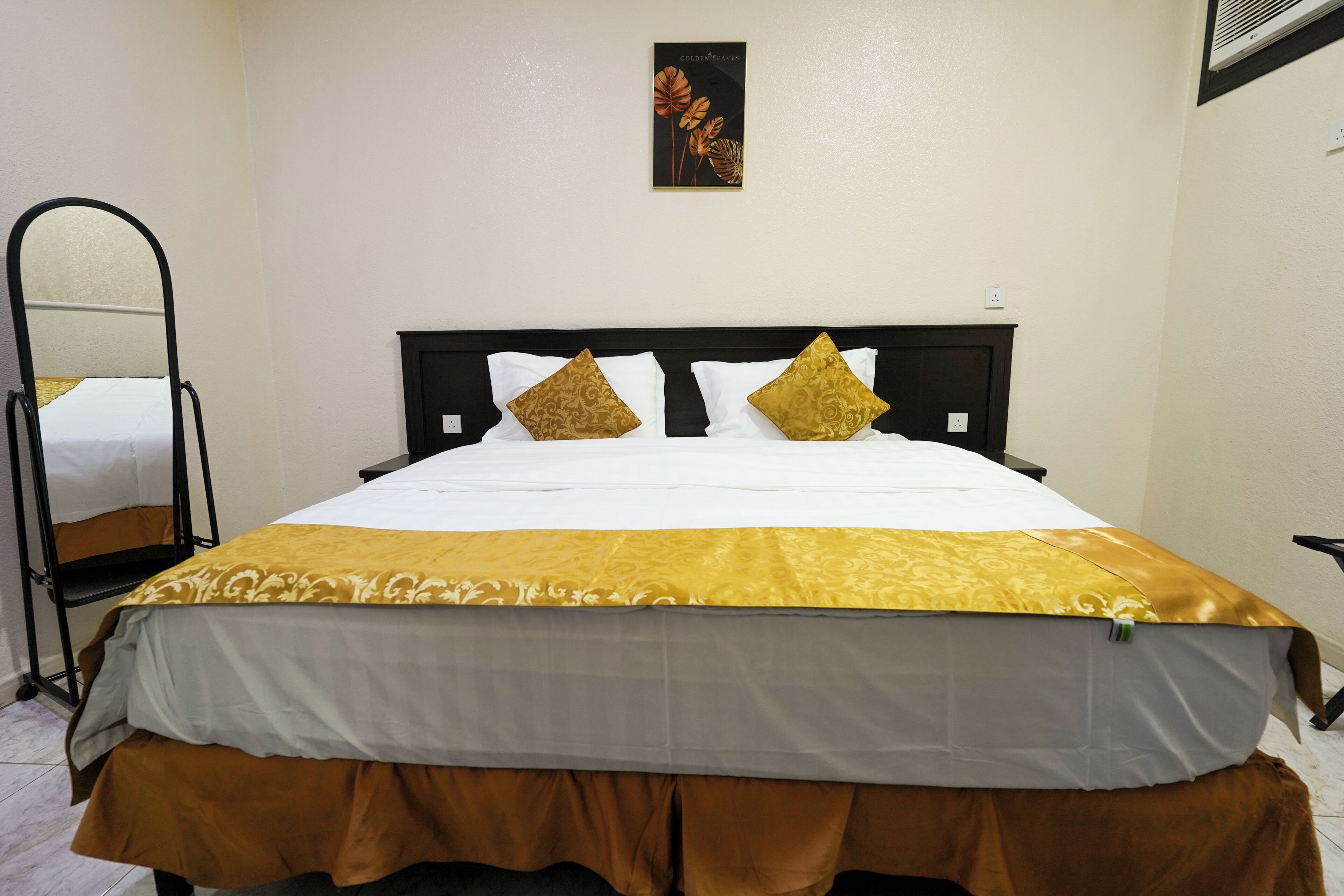 A bed with a white and brown bedspread, two gold pillows, and a black headboard.