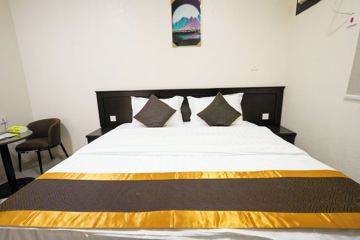 Habitación de hotel con cama, dos almohadas, mesita de noche, silla e imagen colgada en la pared.