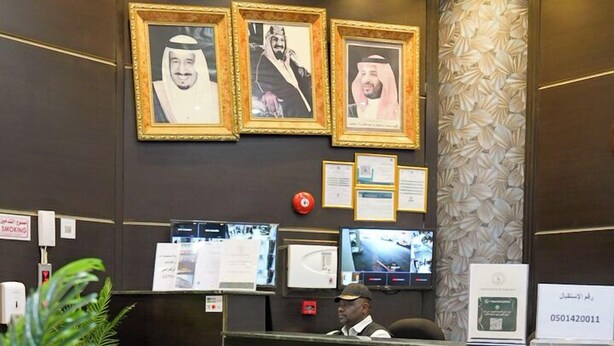 A reception desk with framed portraits, a digital display, and a plant.