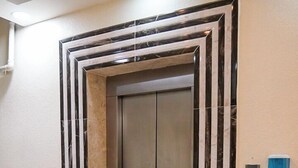 An elevator with a metallic finish, flanked by walls with a striped pattern, and a trash bin to the left.