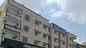 A multi-story building with a sign for 'ASFOUR SERVICED APARTMENTS' and a storefront with Arabic signage.