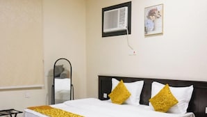 A hotel room with a bed, a nightstand, a mirror, and a wall-mounted air conditioner.