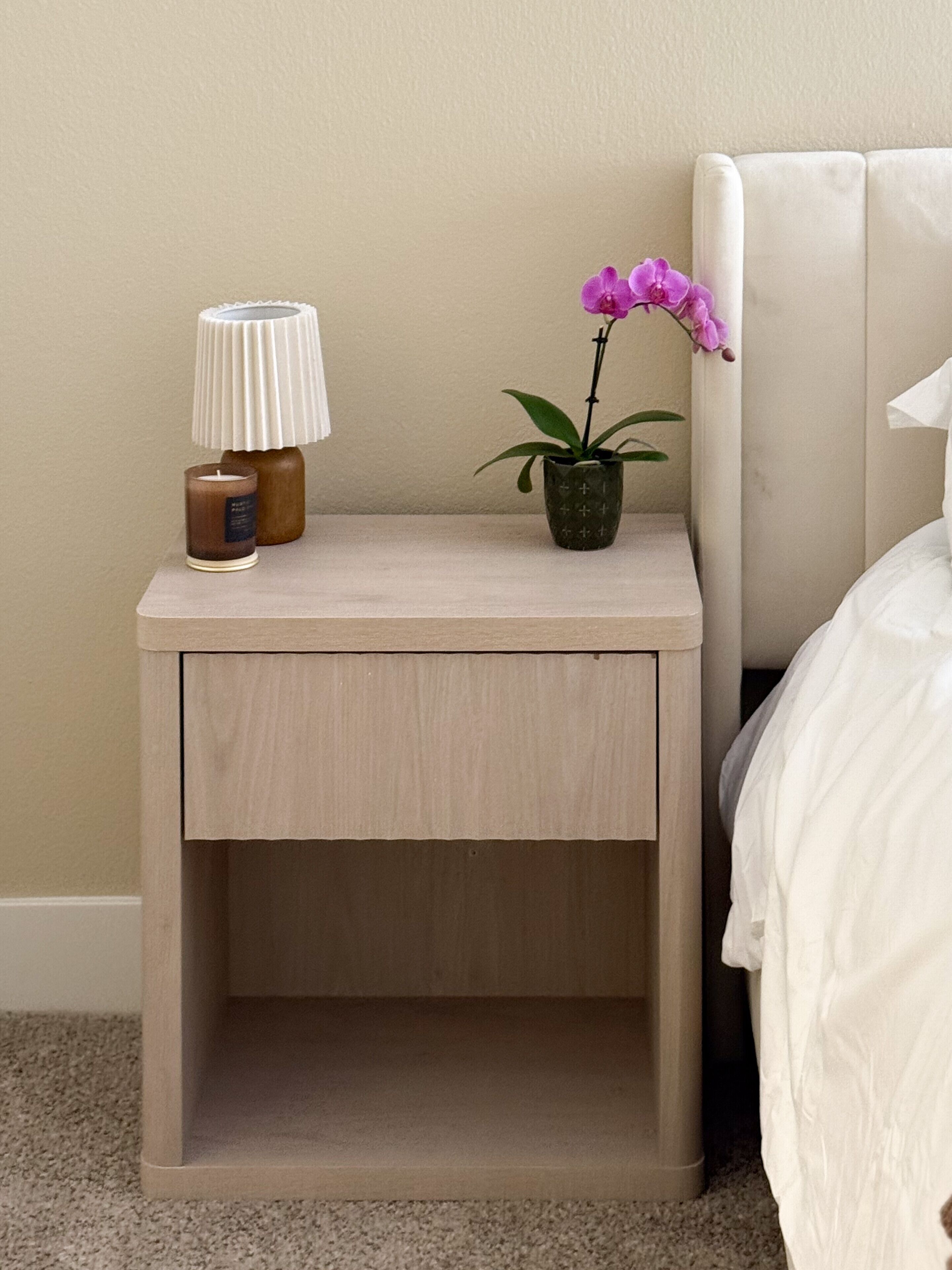 Une table de chevet avec une lampe, une petite plante en pot et une bougie.