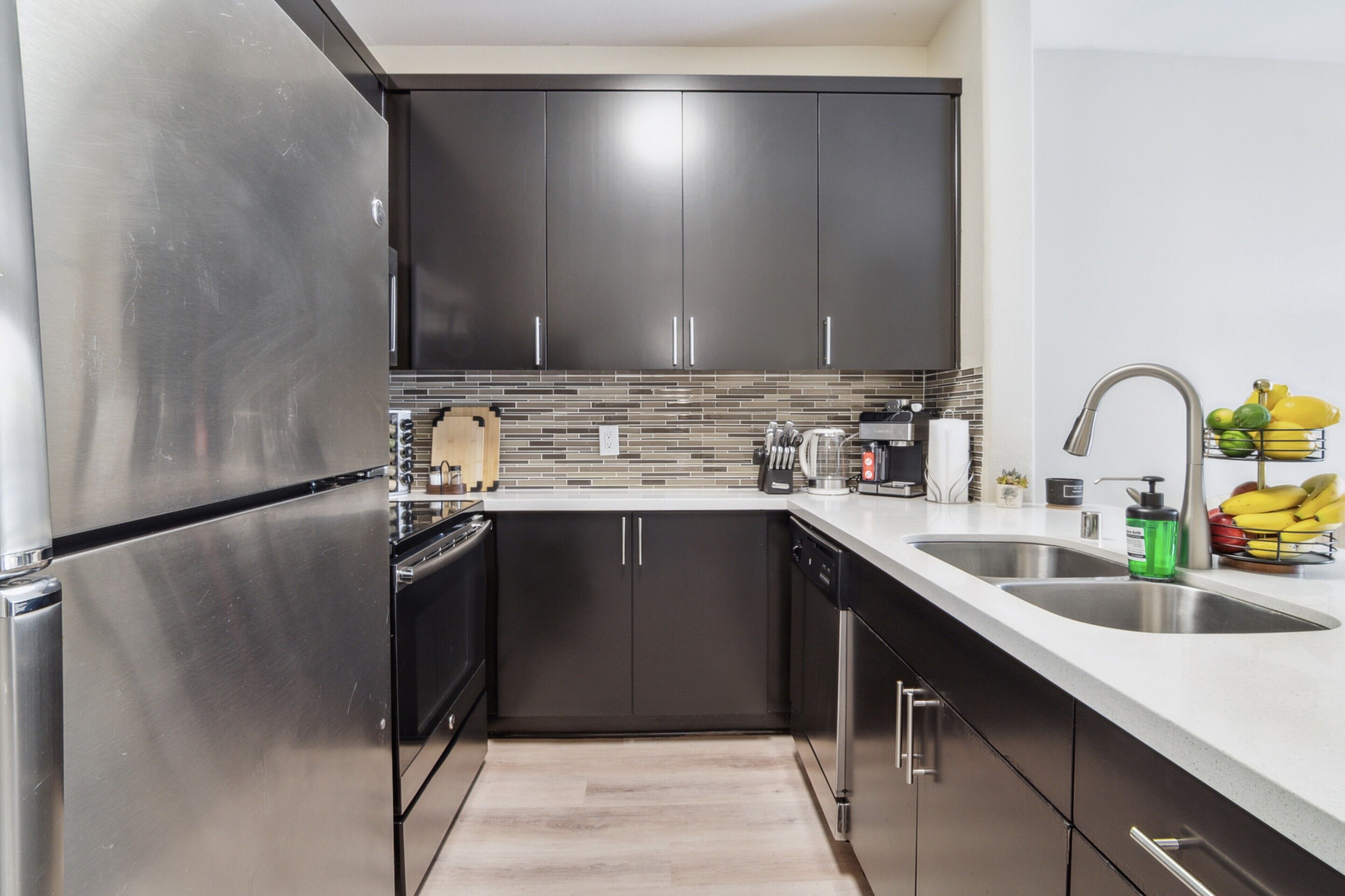 Une cuisine moderne dotée d’appareils électroménagers en acier inoxydable, de meubles de rangement aux couleurs sombres et d’un revêtement mural en carreaux.