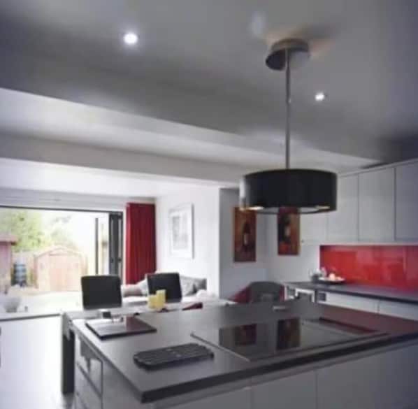 Une cuisine moderne dotée d’un îlot central, de luminaires suspendus et offrant une vue sur l’extérieur.