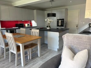 Une cuisine moderne avec des meubles gris, un pare-feu rouge, une table à manger avec des chaises et un canapé gris.
