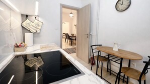 Una cocina moderna con estufa integrada, un comedor con mesa y sillas de madera, y un reloj de pared.