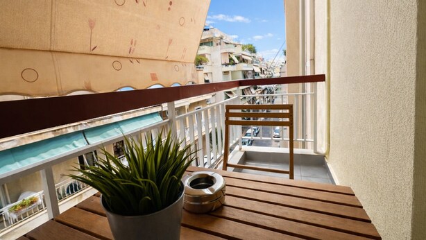 Un balcón con piso de madera, una planta en maceta, una silla de metal y barandilla.