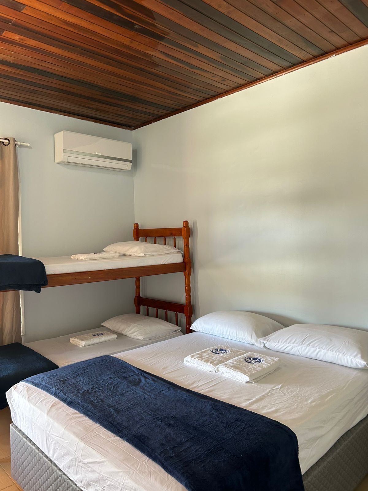 Habitación con literas, techo de madera, unidad de aire acondicionado y una cama con manta azul.