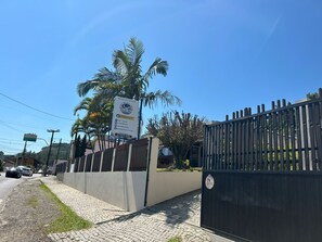 Zona vallada con letrero, palmeras y un camino pavimentado.