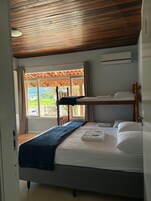 Quarto com beliche, janela com cortinas, ventilador de teto e ar condicionado.