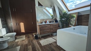 Een moderne badkamer met dakraam, houten kastjes, een witte badkuip en een wastafel met spiegel.