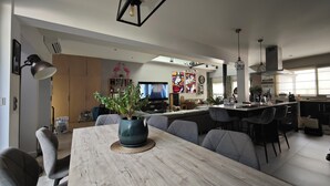 Een ruime woonkamer met een houten eettafel, grijze banken en een keuken met een bar.