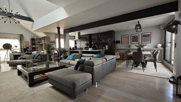 Een ruime woonkamer met een moderne bank, een glazen salontafel, en een eethoek met een tafel en stoelen.