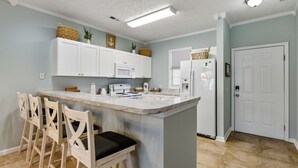 Una cocina con armarios blancos, una isla de mármol, taburetes de bar y un refrigerador.