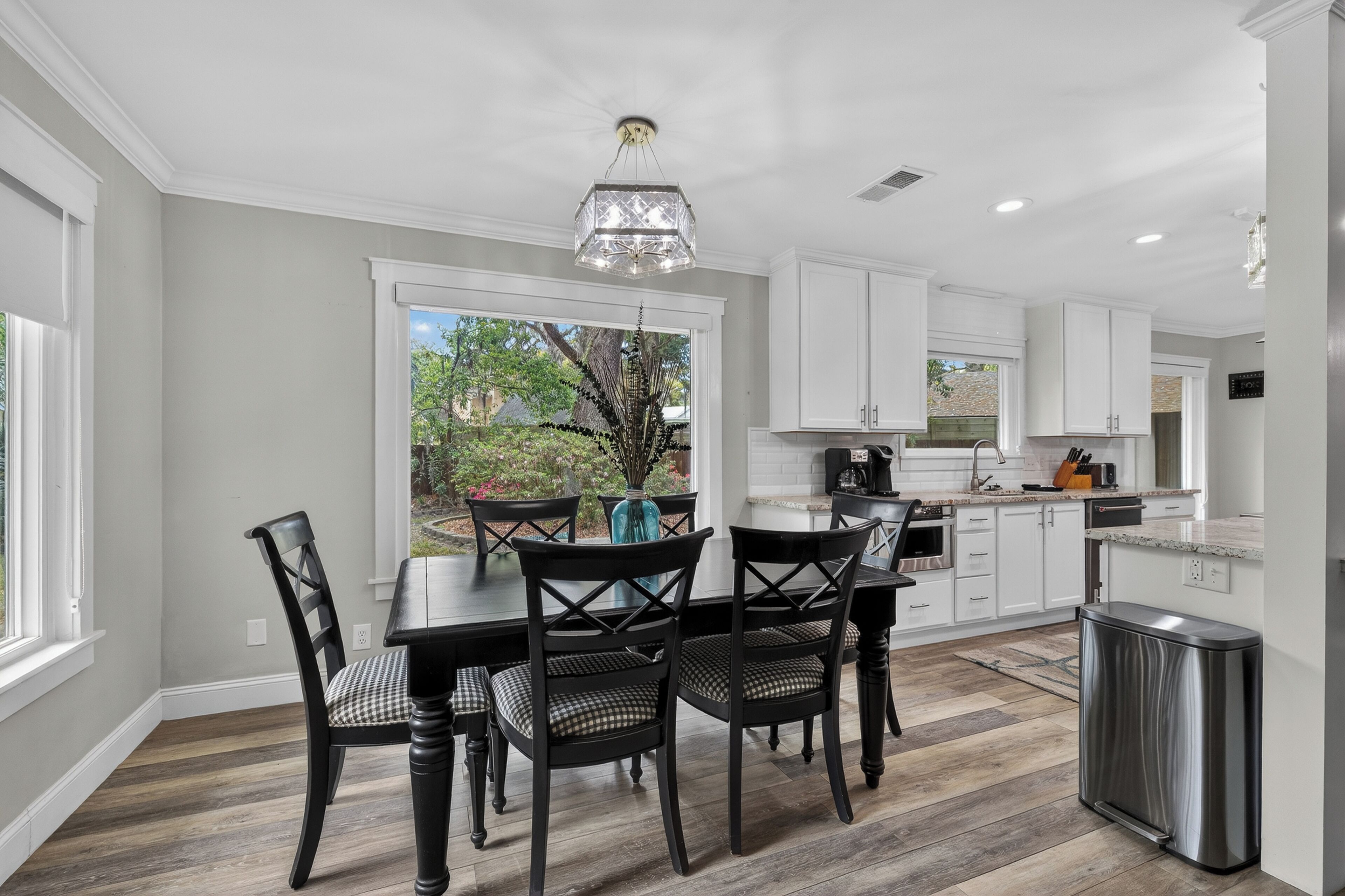 A modern kitchen with white cabinetry, a dining table with chairs, and a view of the outdoors.