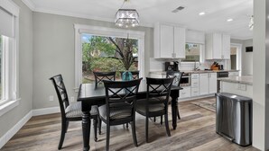 A modern kitchen with white cabinetry, a dining table with chairs, and a view of the outdoors.