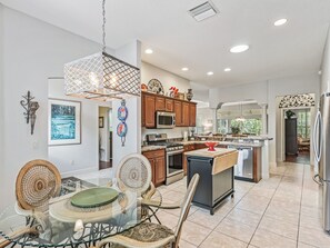 A modern kitchen with wooden cabinets, a central island, and a dining area with a glass table and chairs. - Charming Large 3-bedroom 2 bath house in The Villages. (The Villages)